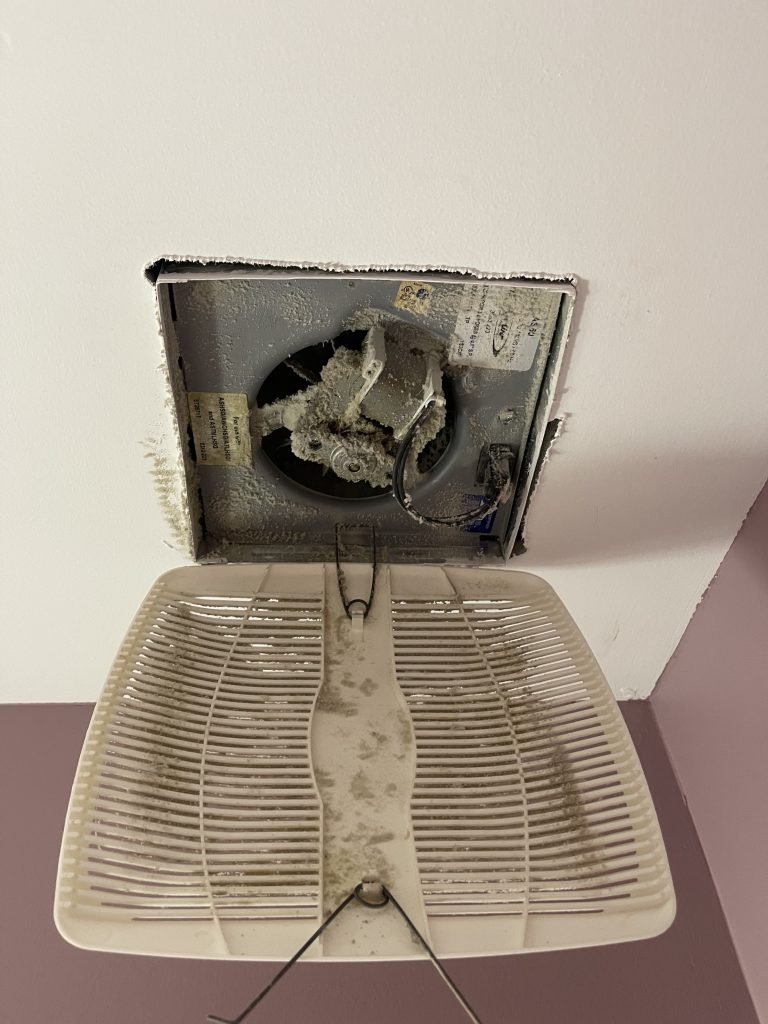 Washroom exhaust fan housing packed with thick dust and lint, cover grille removed